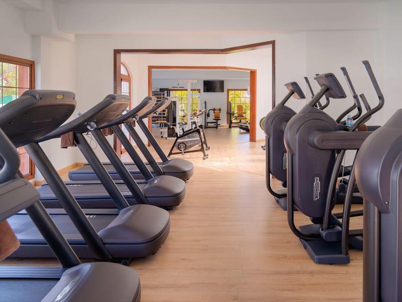 Nowoczesna siłownia z bieżniami i orbitrekami na jasnej drewnianej podłodze.