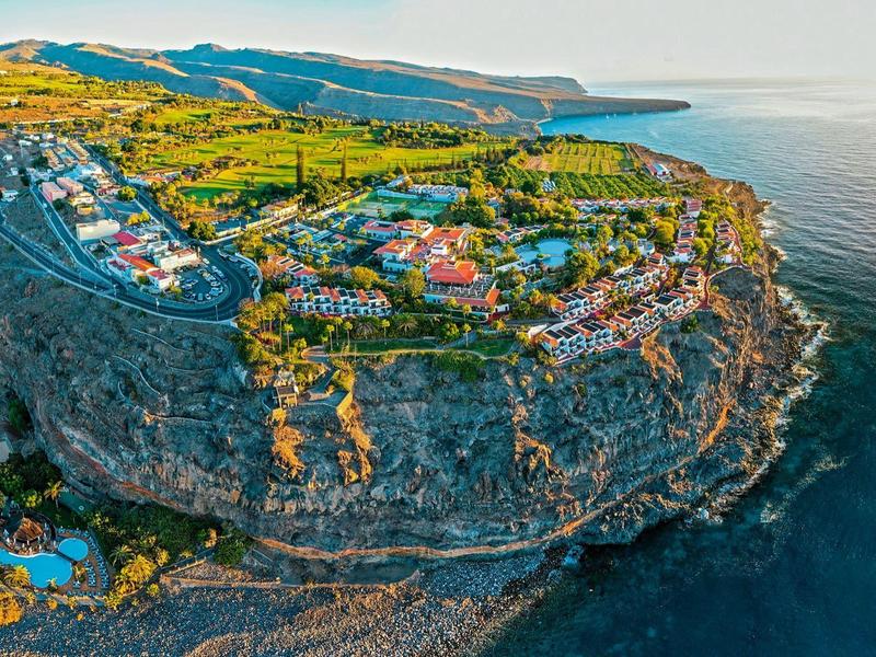 Ośrodek hotelowy na klifie z widokiem na morze i okoliczny krajobraz o zachodzie słońca.