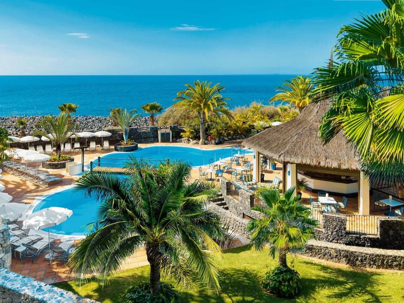 Tropikalny basen hotelowy z palmami i widokiem na niebieskie morze pod czystym niebem.