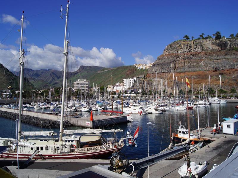 Hafen mit vielen Segelbooten, umgeben von Bergen und blauem Himmel.