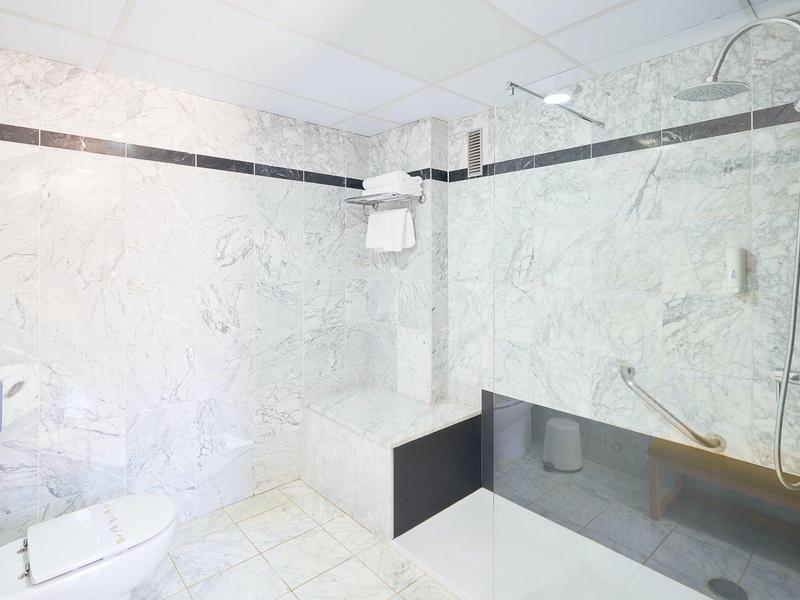 Modernes Badezimmer mit weißem Marmor, dunkler Glasdusche und Wand-WC, helle Lampen und klare Linien.