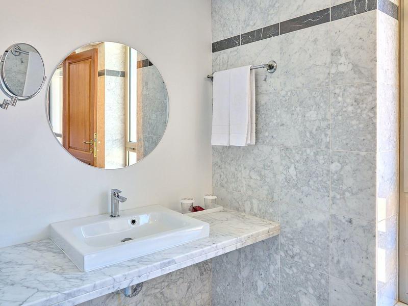 Weißes Waschbecken auf grauer Marmorplatte mit rundem Spiegel und Handtuch an grauer Wand.