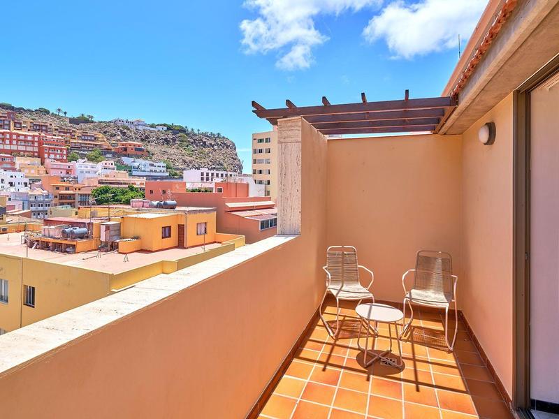 Balkon mit zwei Stühlen und kleinem Tisch, Blick auf bunte Häuser und Hügel bei blauem Himmel.