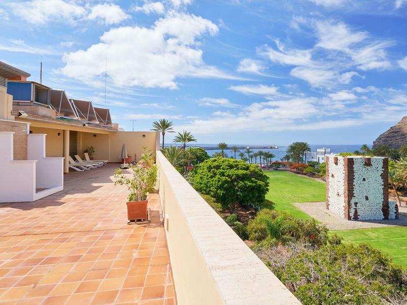 Terrasse mit Fliesen, Blick auf grünen Garten, Palmen und blauen Himmel mit Wolken.