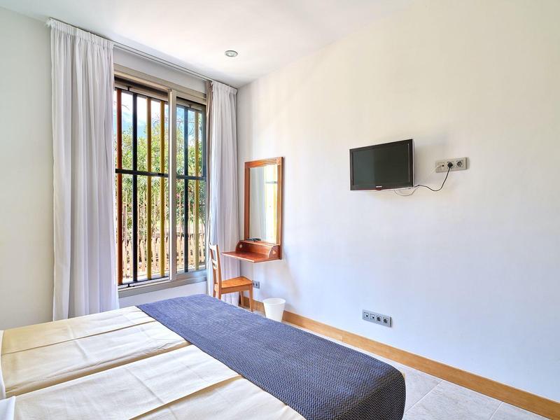 Helles Schlafzimmer mit zwei Betten, großem Fenster mit Vorhängen, Schreibtisch und Wand-TV.