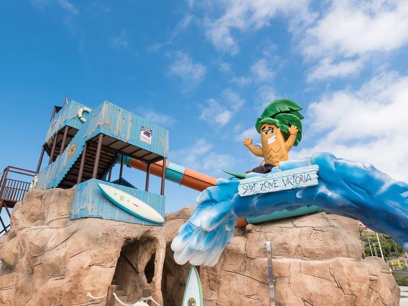 Grote glijbaan met cartoonfiguur en rotsstructuren onder blauwe lucht