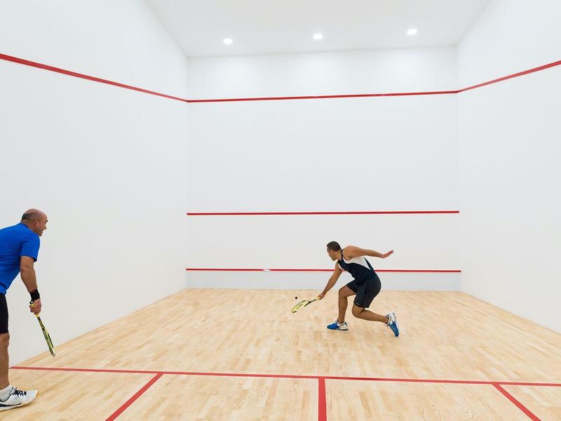 Twee personen spelen squash in een lichte afgesloten baan met rode lijnen.