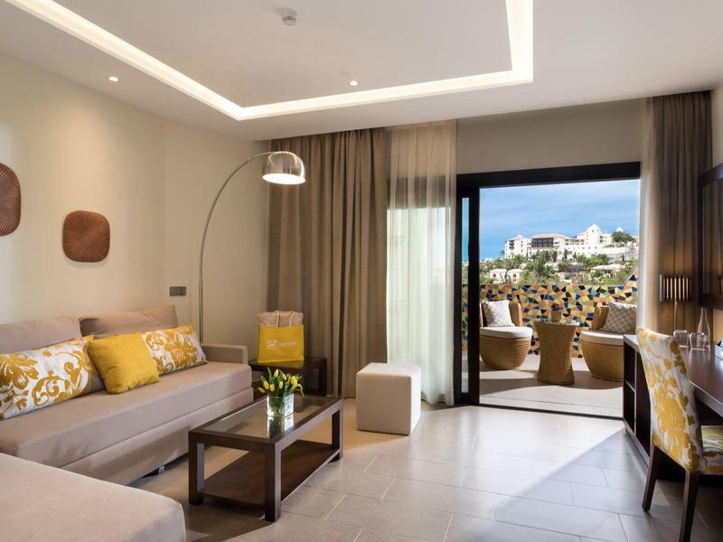 Modern ingerichte hotelkamer met bank, bureau en balkon met uitzicht.