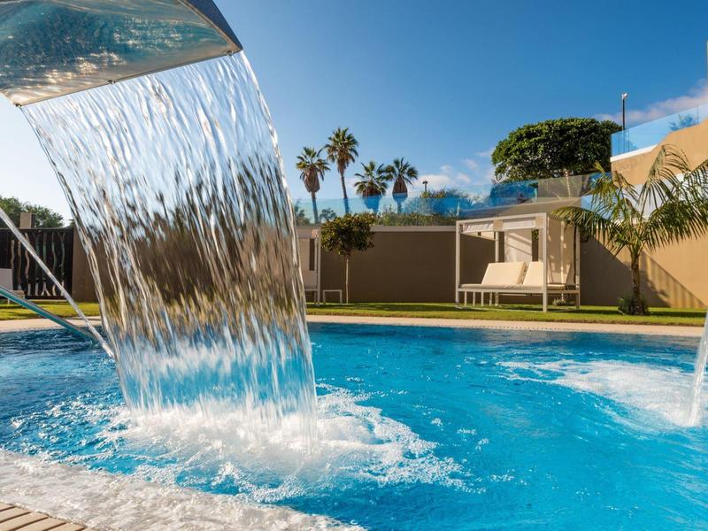 Zwembad met waterval en palmbomen in een zonnige hotelomgeving.