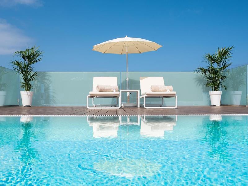 Twee ligstoelen met parasol bij een helder zwembad onder een blauwe lucht.