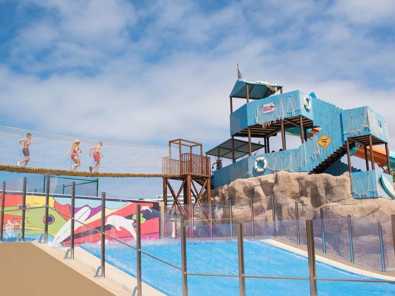 Waterpark met glijbanen in blauw en kleurrijke muurschilderingen onder bewolkte hemel.