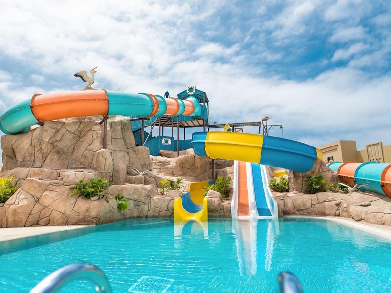Kleurrijk waterglijbaanpark met zwembad, rotsen en bewolkte lucht op de achtergrond.
