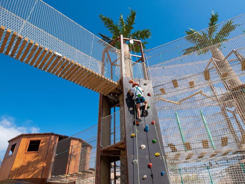Persoon klimmend op een klimwand in een buiten avonturenpark bij een blauwe lucht.