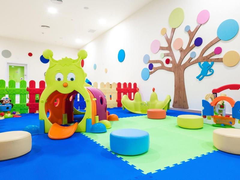 Kleurrijke indoor speelruimte voor kinderen met glijbaan, kussens en speelgoed in een heldere kamer.