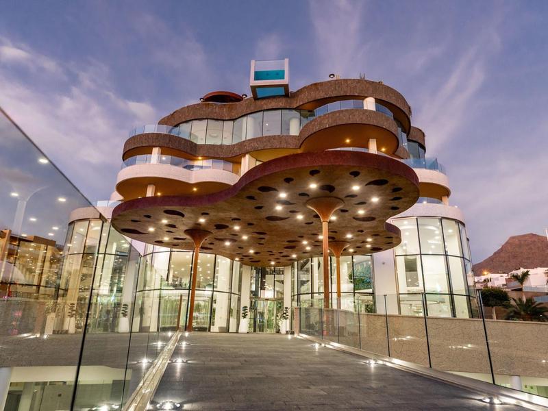 Modern hotel met gebogen architectuur en grote glazen gevels bij schemering.