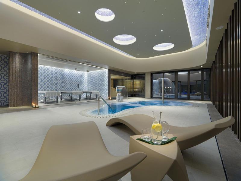 Moderne overdekte zwembadruimte met ligstoelen en een drankje op het bijzettafeltje.