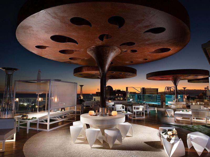 Avondterras op het dak met futuristische, paddenstoelvormige zonneschermen en zithoeken.