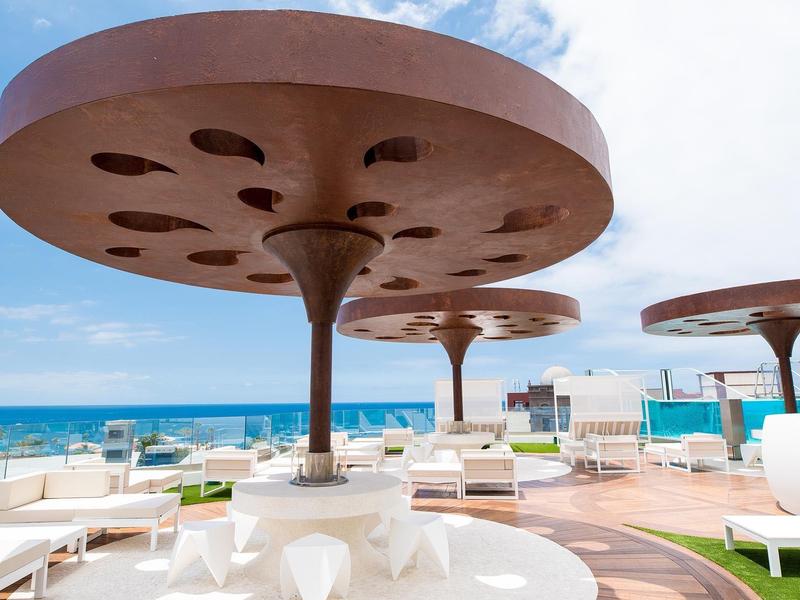 Moderne ronde zonneschermen op een terras met wit meubilair en uitzicht op zee.