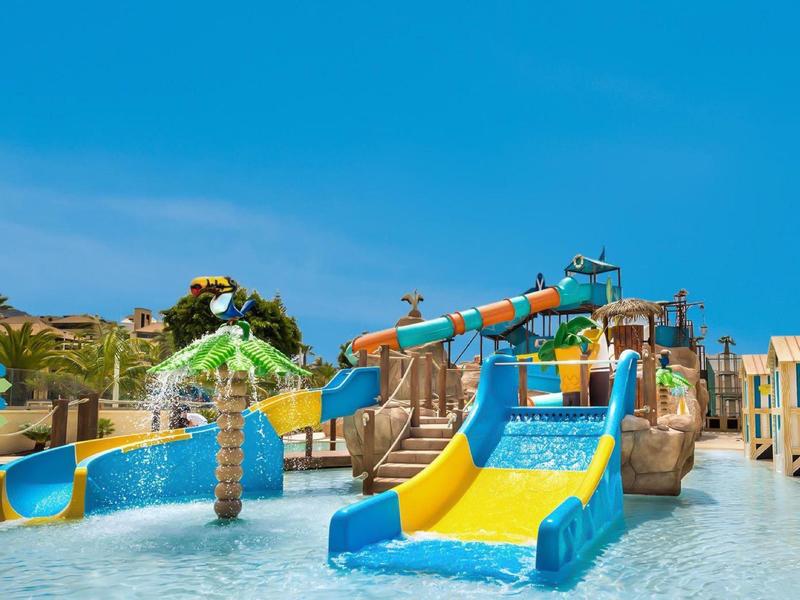 Kleurrijke waterspeeltuin met glijbanen en waterkanonnen onder een blauwe lucht.