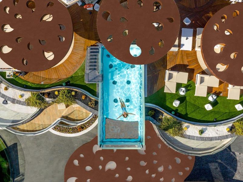 Luchtfoto van een zwembad met blauwe glijbaan en ronde parasols bij een hotelcomplex.