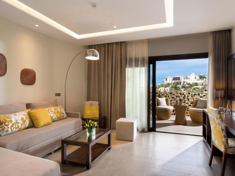 Lichte, moderne hotelwoonkamer met bank, salontafel en toegang tot terras met uitzicht.