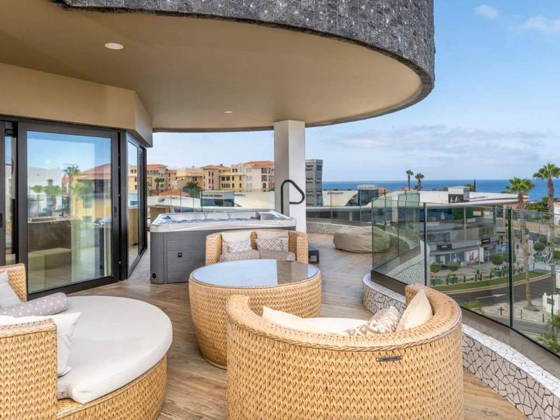 Balkon van hotelkamer met ronde rotan stoelen, zeezicht en moderne architectuur.