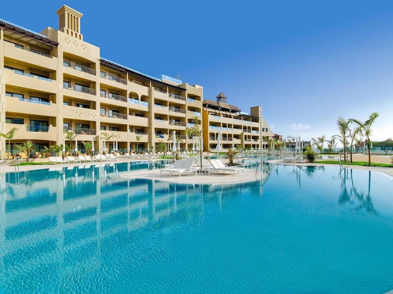 Groot hotelgebouw met buitenzwembad en heldere lucht op de achtergrond.