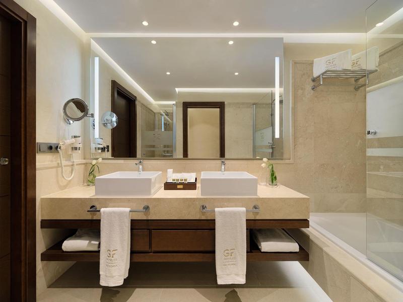 Modern hotelbadkamer met grote wastafel, handdoeken en bad met glazen wand.