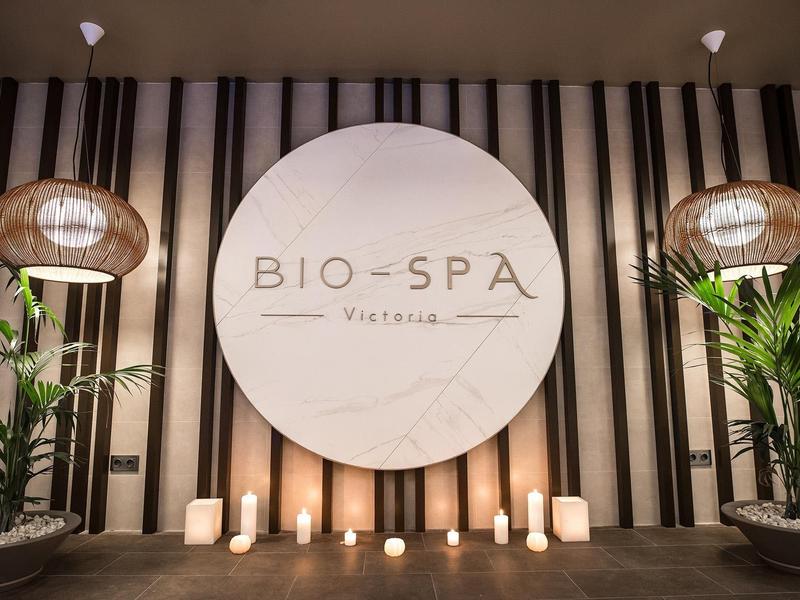 Elegante spa-ingang met rond logo, kaarsen en groene planten voor een gestreepte muur.