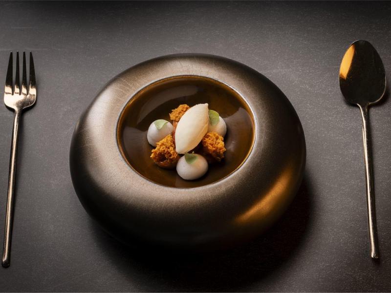 Elegant dessert met verschillende texturen op zwart bord en bestek.