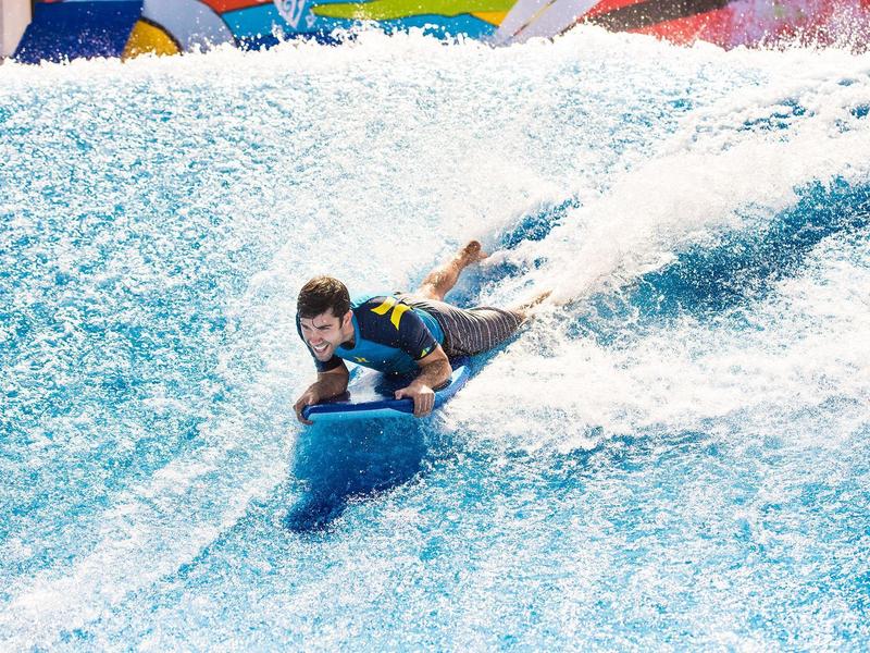 Jongen surft op een indoor golfrutsche met blauw water en kleurrijke achtergrond.