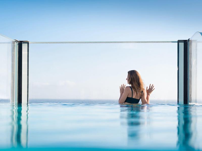 Vrouw in zwembad kijkt uit over de oceaan op een heldere, zonnige dag.