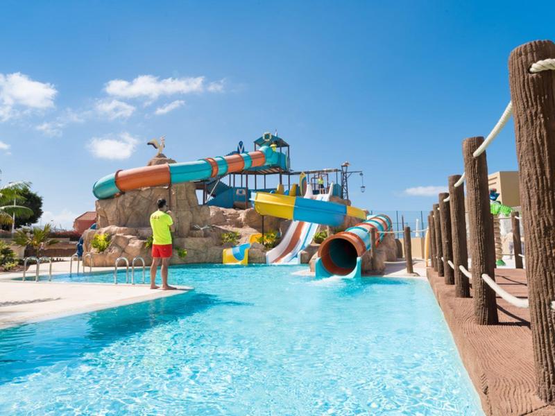 Waterpark met glijbanen, zwembad en bezoekers op een zonnige dag met blauwe lucht.
