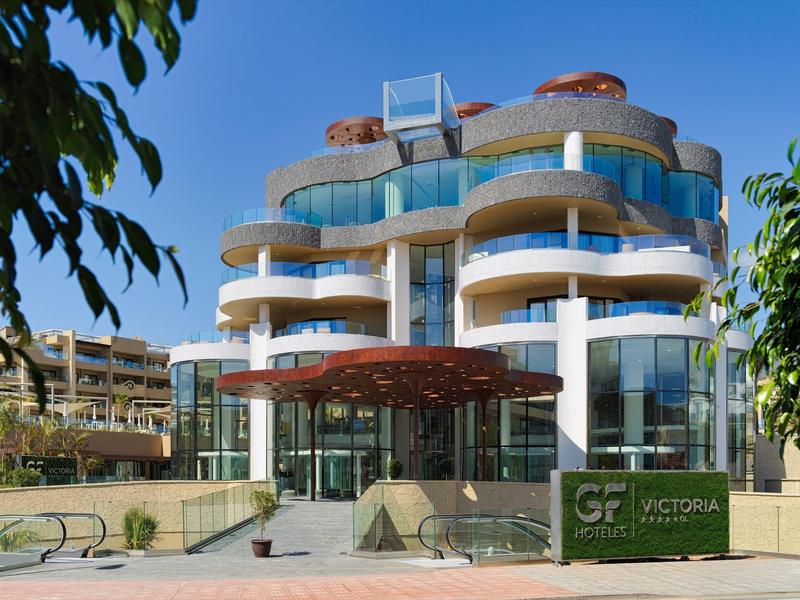 Modern hotelgebouw met ronde ingang en blauwe glasbalkons onder een zonnige hemel.