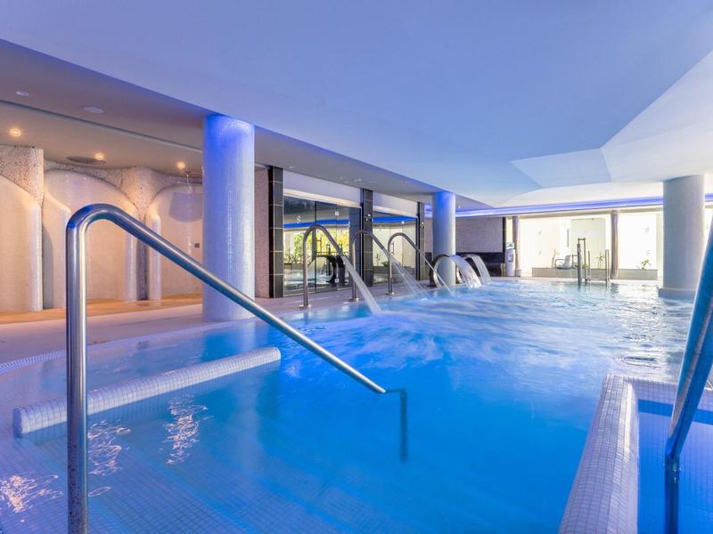 Indoor hotel pool with blue lighting and large windows showing outside view.