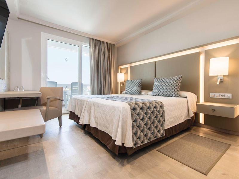 Modern hotel room with a large bed, bedside lamps, window, and a chair by the desk.