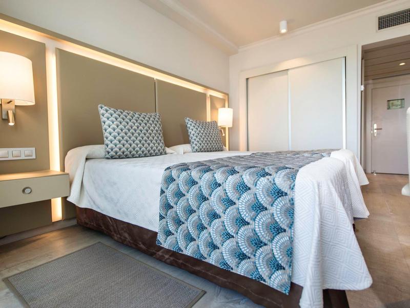Modern hotel room with a bed, light blue quilt, and bedside lamps.