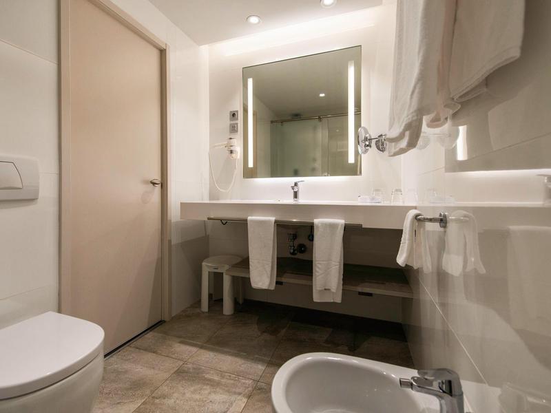 Modern bathroom with a large mirror, white sink, toilet, and bidet in a hotel room.
