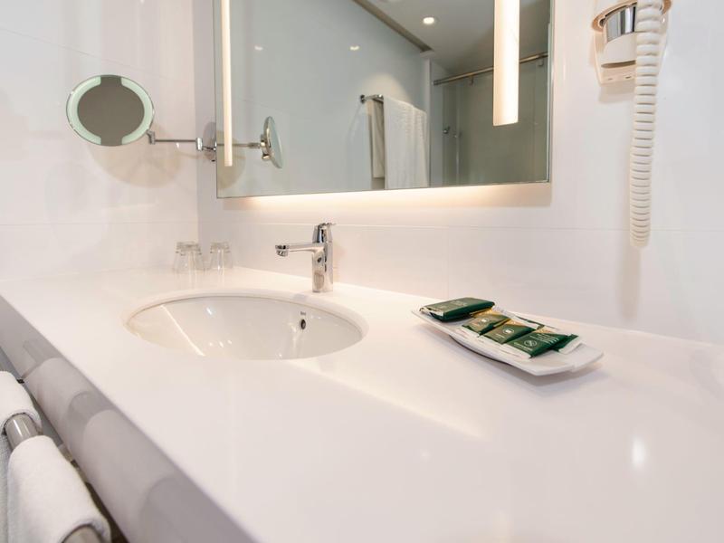 Modern hotel bathroom sink area with white countertop and toiletries.