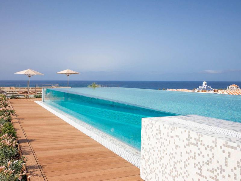 Infinity pool with wooden deck and umbrellas overlooking the sea on a clear day