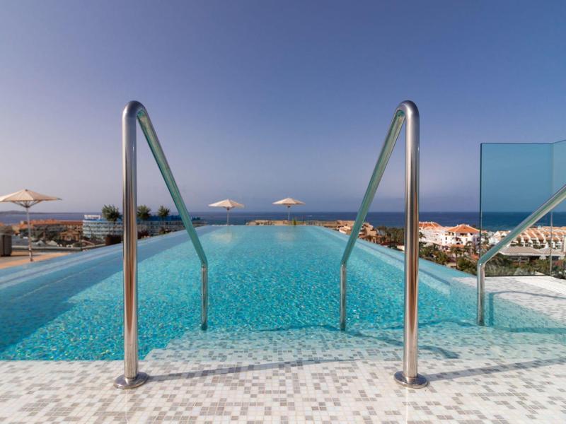 Infinity pool with clear water overlooking the ocean under a blue sky.
