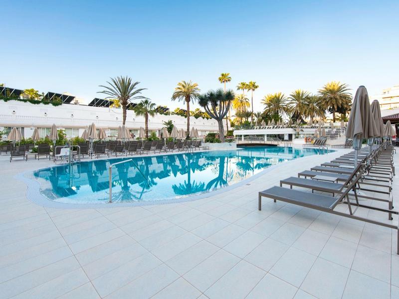Outdoor pool area with sun loungers, palm trees, and clear blue sky at a resort.