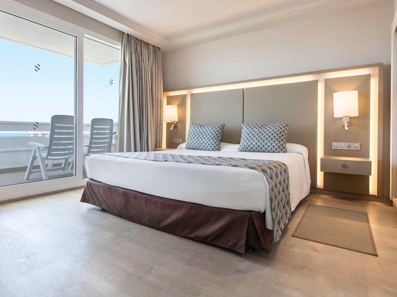 Modern hotel room with large bed and balcony overlooking the sea.