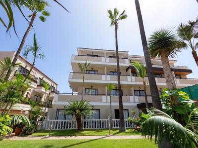 Moderne meerlaagse hotelgebouwen omgeven door tropisch groen en palmbomen onder een blauwe lucht.