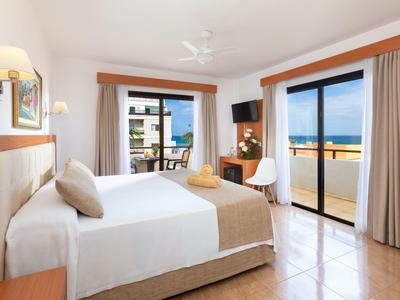 Lichte hotelkamer met tweepersoonsbed, balkon en zeezicht.