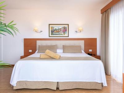 Licht ingericht hotelkamer met groot bed, nachtkastjes en decoratieve afbeelding aan de muur.