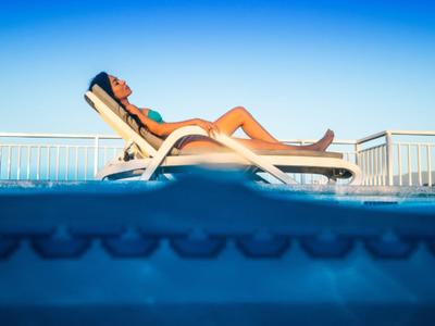 Woman relaxing on lounge chair by pool under clear sky