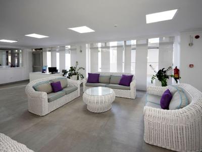 Bright lounge with white rattan furniture and purple cushions in a modern hotel.