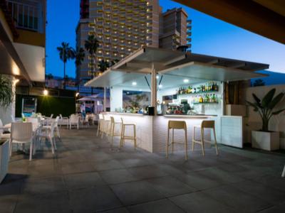 Espace bar extérieur moderne avec mobilier blanc et immeubles en arrière-plan au crépuscule.