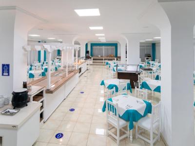 Salle à manger lumineuse avec mobilier blanc et nappes turquoise dans un hôtel.